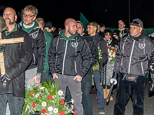 Personen in Kleidung der Partei "Der III. Weg" Nachts auf einem rechten Aufmarsch, Vor ihnen liegt ein Blumenstrauß.