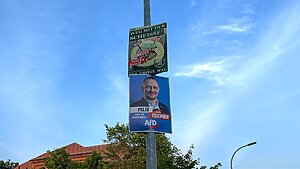 Zwei Plakate hängen übereinander an einem Laternenpfahl, eins ist von der AfD, das andere vom III. Weg