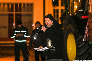 Eine Person spricht in ein Mikrofon. Im Hintergrund steht ein Traktor.